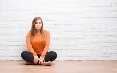 Young adult woman sitting on the floor in autumn over white brick wall with a confident expression on smart face thinking serious clipart