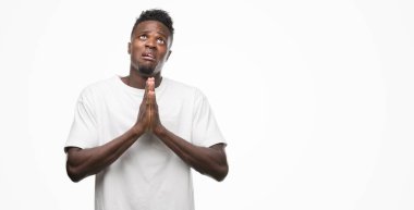 Yalvarıyor ve umut ifade yüzünde çok duygusal ve endişe ile birlikte elleriyle dua beyaz t-shirt giyen genç Afro-Amerikan adam. Bağışlanmak. Din kavramı.