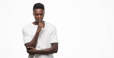 Dudaklarında parmak ile sessiz olmanı beyaz t-shirt giyen genç Afro-Amerikan adam. Sessizlik ve gizli kavramı.