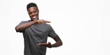 Büyük ve büyük boy işaret, ölçü birimi sembol gösteren ellerle eller gri t-shirt giyen genç Afro-Amerikan adam. Kameraya bakarak gülümsüyordu. Ölçüm kavramı.