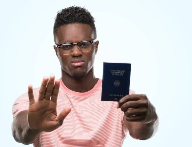 Alman pasaportu ile tutan genç Afro-Amerikan adam dur işareti ile ciddi ve kendine güvenen ifade, savunma hareketi yaparken el açmak