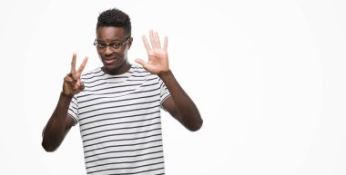 Gözlük ve gösterilen ve parmakları ile işaret lacivert t-shirt giyen genç Afro-Amerikan adam kendinden emin ve mutlu gülümseyerek süre yedi numara.