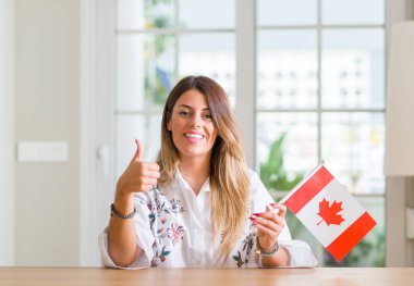 Genç kadın evde Kanada bayrağı ok işareti yapıyor büyük gülümseme ile mutlu tutarak başparmak yukarı parmaklarıyla, mükemmel işareti