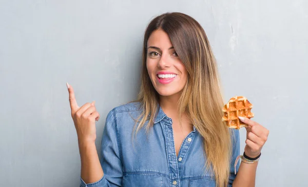 灰色のグランジ壁側の手と指で指す非常に幸せなベルギー ワッフルを食べる若い成人女性 — ストック写真