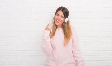 Müzik ve dans çok mutlu el ve parmak ile işaret kulaklık takmış beyaz tuğla duvarın üzerinden Genç Yetişkin kadın