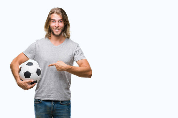 Young handsome man with long hair over isolated background holding football ball very happy pointing with hand and finger