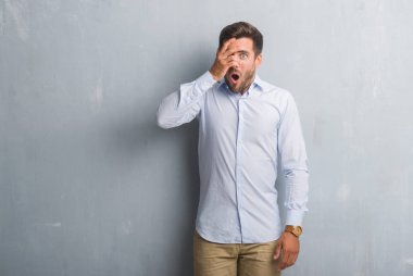 Mahcup ifadeyle parmaklarımın arasından seyir yakışıklı genç iş adamı yüz ve gözler el ile kapsayan şok şık gömlek bakmak giyen gri grunge duvarın üzerinden.