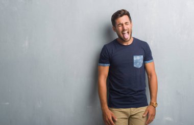 Yakışıklı delikanlı dilini gri grunge duvarın üzerinden out komik ifade ile mutlu. Duygu kavramı.