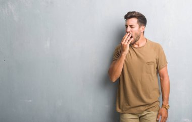 Yakışıklı genç gri grunge duvarın üzerinden esneme yorgun kapsayan ağız el ile sıkılmış. Restless ve uyku hali.