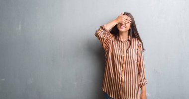 Genç esmer kadın gülümsüyor ve gözleri için sürpriz kapsayan yüz el ile gülüyor grunge gri duvar yüzünden. Kör kavramı.