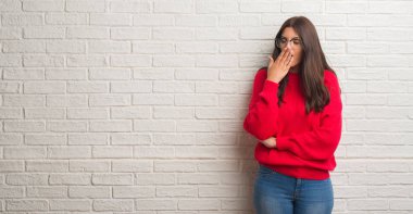 Beyaz tuğla duvardan esneme sıkılmış duran genç esmer kadın kapsayan ağız el ile yorgun. Restless ve uyku hali.