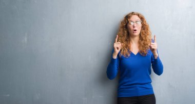 Genç Kızıl saçlı kadın gri grunge duvarın üzerinden hayran ve yukarıya bakıp parmakları ile işaret şaşırttı ve silah kaldırdı.