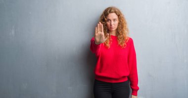 Gri grunge duvar kırmızı kazaklı elin avuç durağı şarkı yapıyor giyen genç Kızıl saçlı kadın. Negatif ve ciddi bir jest yüz ifadesiyle uyarı.