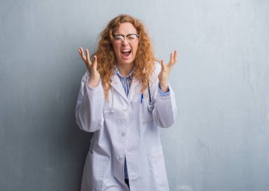 Genç redhead doktor kadın kutluyor kızgın ve silah ile başarı için deli bir palto giyiyor gri grunge duvarın üzerinden kaldırdı ve heyecanlı çığlık gözler kapalı. Kazanan kavramı