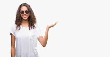 Neşeli sunulması ve kameraya bakarak avucunun ile işaret gülümseyen güneş gözlüğü takmış genç İspanyol kadın.