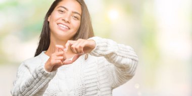 Kalp simgesi ve elleriyle şekil gösterilen aşık gülümseyen izole arka plan üzerinde kış kazak giyen genç güzel Arap kadın. Romantik kavramı.