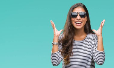 Genç güzel Arap kadın deli ve çığlık kaldırdı ve kapalı gözleri heyecanlı silah ile başarı için deli kutluyor izole arka plan üzerinde güneş gözlüğü takıyor. Kazanan kavramı