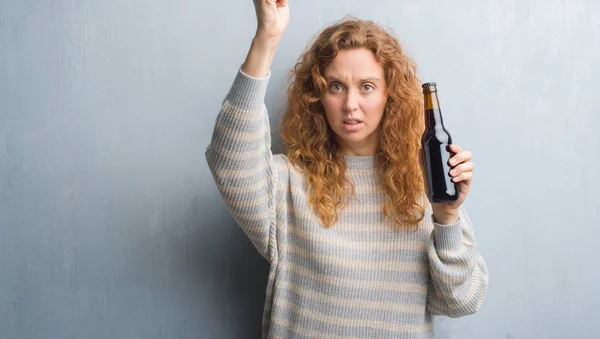 Joven Pelirroja Sobre Pared Grunge Gris Sosteniendo Botella Cerveza Molesta — Foto de Stock