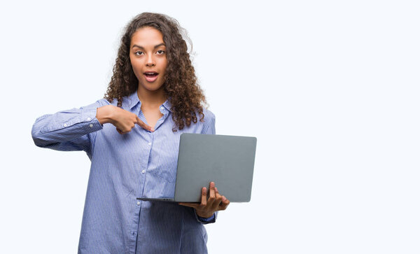 Young hispanic woman holding computer laptop with surprise face pointing finger to himself