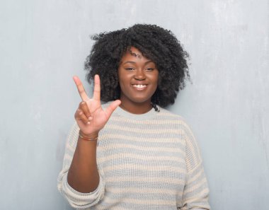 Genç Afro-Amerikan artı boyutu kadın gösterilen ve parmakları ile işaret Kazak giyen gri grunge duvarın üzerinden üçüncüsü ise kendinden emin ve mutlu gülümseyerek.