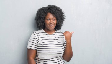Genç Afro-Amerikan artı boyutu kadın arıyorum ve başparmak yanında yukarıyı mutlu yüz ile gülümseyen gri grunge duvarın üzerinden.
