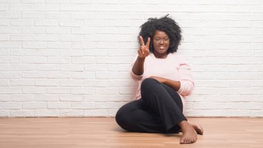 Evde yerde gösterme ve işaret parmakları ile oturan genç Afro-Amerikan kadın ikincisi ise kendinden emin ve mutlu gülümseyerek.