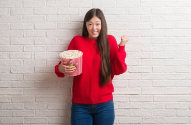 Duygu tezahürat Genç Çinli kadın gurur çığlık ve zafer ve başarı çok heyecanlı, kutluyor pop Mısır yeme tuğla duvarın üzerinden