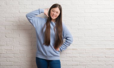 Üzerinde beyaz tuğla duvar gülümseyen kadın genç Chinise el ve parmak telefonda konuşmak ile telefon jest yapıyor. Kavramları iletişim.