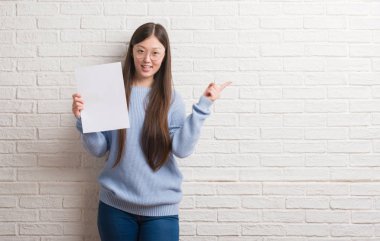 Boş kağıt çok mutlu el ve parmak ile tarafına işaret tutan tuğla duvarın üzerinden Genç Çinli kadın
