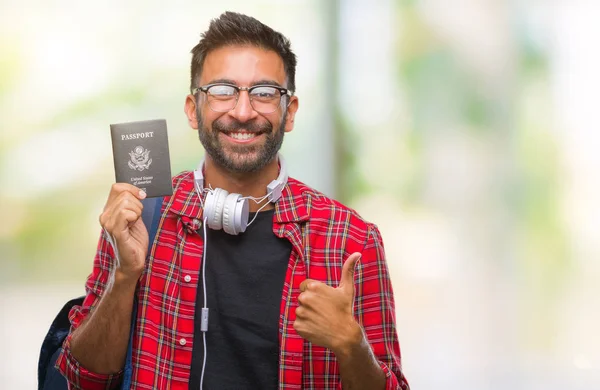 のアメリカのパスポートを保持している大人のヒスパニック学生男笑顔の サイン 優秀な兆候を親指をやって幸せな背景を分離しました — ストック写真