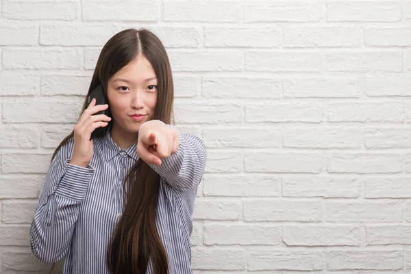 Young Chinese Woman Brick Wall Talking Phone Pointing Finger Camera — Stock Photo, Image