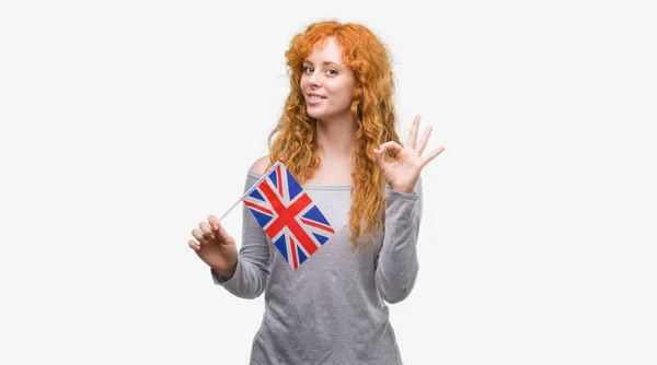 優秀なシンボルの指で サインをしている若い赤毛の女性はイギリスの旗を保持しています — ストック写真