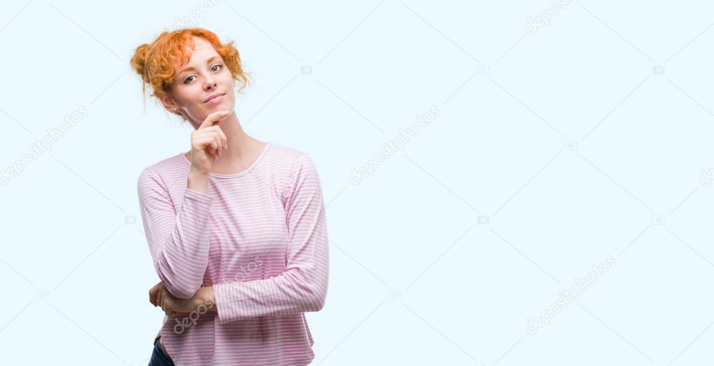 Young redhead woman looking confident at the camera with smile with crossed arms and hand raised on chin. Thinking positive.