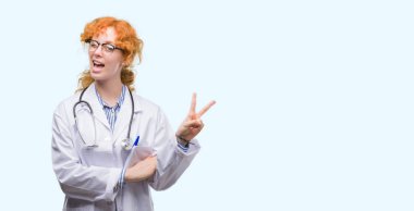 Mutlu yüz zafer işareti yaparken kameraya göz kırpıyor ile gülümseyen Doktor üniforması giyen genç redhead kadın. İki numaralı.