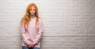 Tuğla duvar şüpheci ve gergin duran genç Kızıl saçlı kadın çatık sorunu nedeniyle üzgün. Negatif kişi.