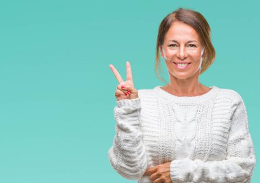 Mutlu yüz zafer işareti yaparken kameraya göz kırpıyor ile gülümseyen izole arka plan üzerinde kış kazak giyen orta yaş üst düzey İspanyol kadın. İki numaralı.