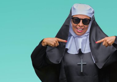 Orta yaş üst düzey Katolik Rahibe kadın yüzünde gülümseme ile kendinden emin görünüyorsun, kendini gururlu ve mutlu parmakları ile işaret izole arka plan üzerinde güneş gözlüğü takıyor.