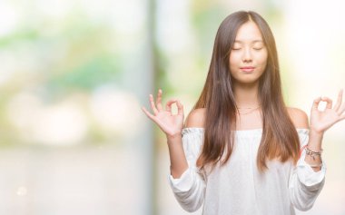 Genç Asyalı kadın izole arka plan üzerinde dinlenmek ve gülümseyen gözlerle parmak ile meditasyon jest yapıyor kapalı. Yoga kavramı.