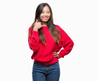 İşin gülümseyen izole arka plan üzerinde kış kazak giyen genç Asyalı kadın telefon hareketi ile el ve parmak telefonda konuşuyor gibi. Kavramları iletişim.