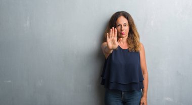 Orta yaş İspanyol kadın stop yapıyor gri grunge duvardan ayakta elin avuç ile şarkı. Negatif ve ciddi bir jest yüz ifadesiyle uyarı.