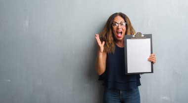 Gri grunge duvar panosu çok mutlu ve heyecanlı, kazanan ifade büyük gülümseme ile çığlık zaferini kutluyor holding üzerinde duran ve ellerini kaldırdı orta yaş İspanyol kadın