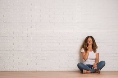 Sessizlik, gizli kavramı orta yaş İspanyol kadın beyaz tuğla duvar kapağı ağız elle hata, korku, ifade için utanç ile şok yüzünden korkuyor