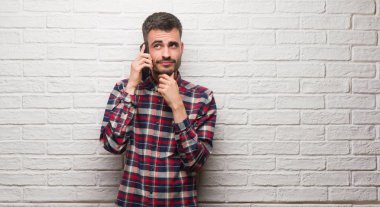 Üzerinde telefon duran beyaz tuğla duvar ciddi bir yüz düşünme üzerinde ilgili soru, çok karışık fikir konuşan genç yetişkin adam