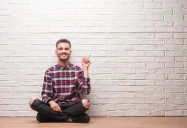 El ve parmak ile tarafına işaret çok mutlu beyaz tuğla duvar üzerine oturan genç yetişkin adam