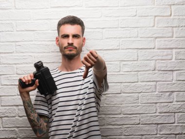 Genç adam tutarak kamerayı kızgın yüzü, eksi işareti aşağı antipati başparmak ile gösterilen, ret kavramı ile beyaz tuğla duvarın üzerinden ayakta filme