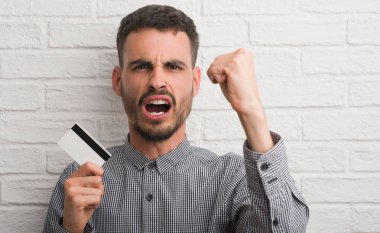 Tuğla duvar holding kredi kartı rahatsız genç yetişkin adam ve boşa çıkarmak ile öfke, çılgın ve yükseltilmiş eliyle diye bağıran öfke kavramı bağırarak.