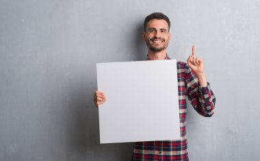 Genç yetişkin adam tuğla üzerinde tutarak afiş bir fikirle sürpriz duvar veya gülen yüz, bir numara ile işaret parmağı soru