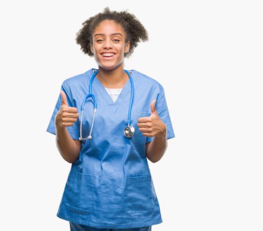 Genç afro Amerikalı doktor kadın izole arka plan başarı işareti başparmak gülümseyen ve mutlu el ile olumlu hareketi yapıyor. Neşeli bir ifadeyle, kazanan jest kameraya bakıyor.