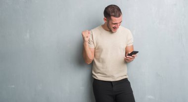 Gurur çığlık ve zafer ve başarı çok heyecanlı, kutluyor smartphone kullanarak bir ileti duygu tezahürat manifatura gri grunge üzerinde beyaz delikanlı duvar