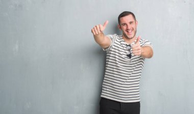 Gri grunge duvar onaylama üzerinde beyaz delikanlı el ile pozitif jest yapıyor gülümseyen ve başarı için mutlu yaşasın. Kamera, kazanan jest arıyorsunuz.